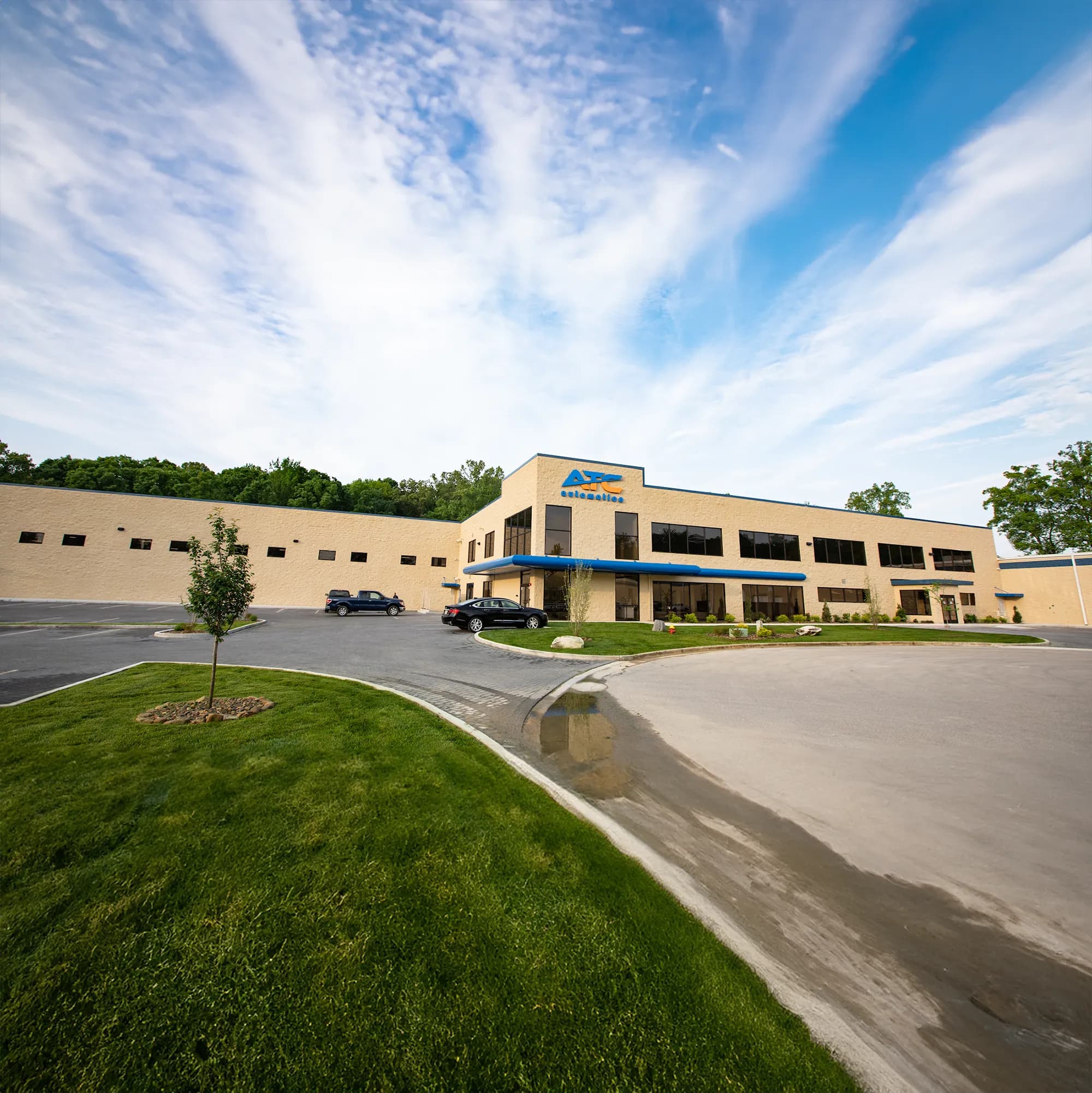 The front of a tan building with dark brown windows with a parking lot in front.