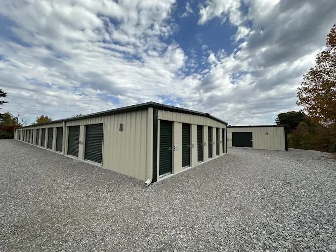 A one story tan storage building with green roll up garage doors.