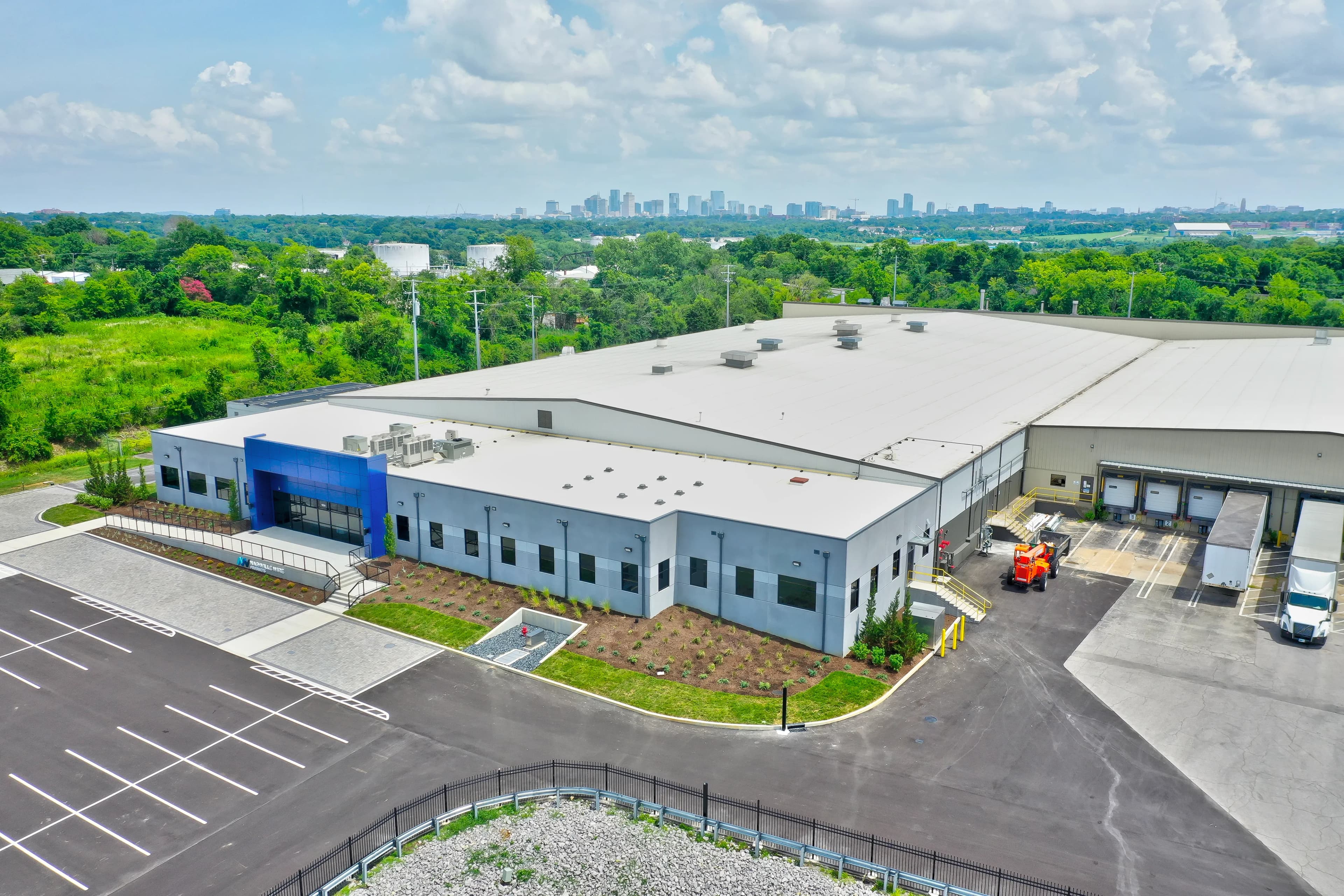 Aerial view of a gray and blue building with a large warehouse attached in the back, the nashville skyline in the background.